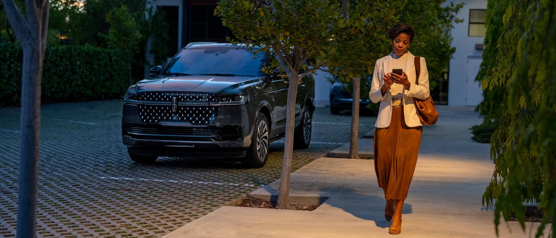 A woman accesses an app on her phone as she walks away from her parked 2027 Lincoln Navigator® SUV