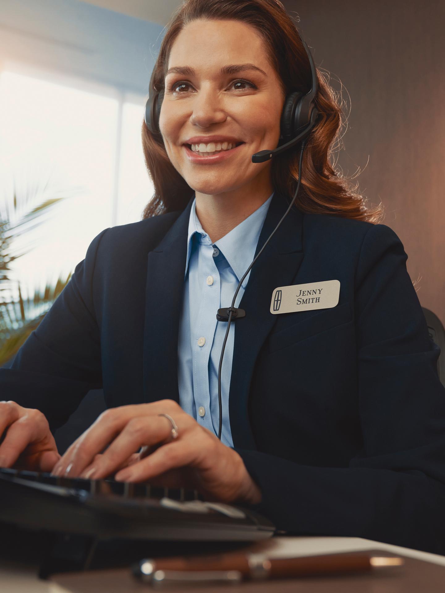 A support agent in a headset types at a desk with the Lincoln logo visible in the background
