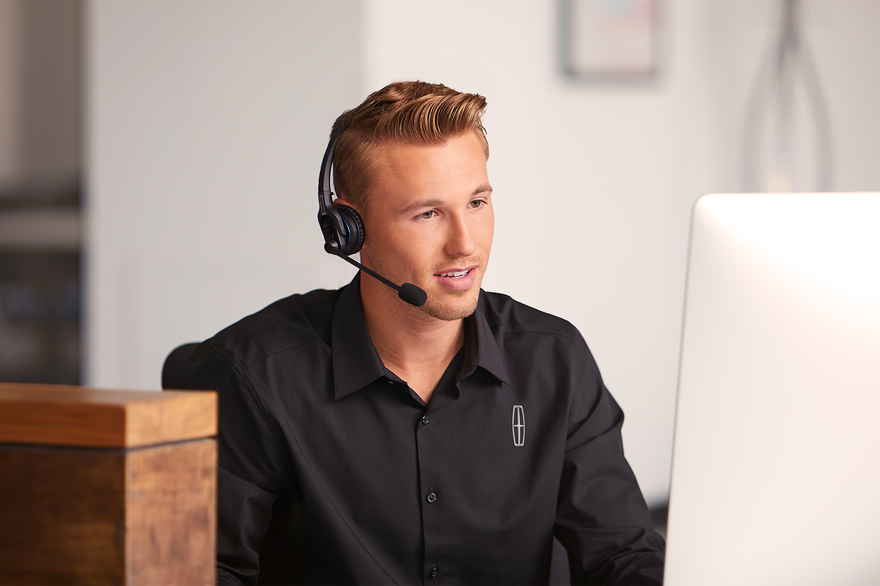 A support agent in a headset types at a desk with the Lincoln logo visible in the background