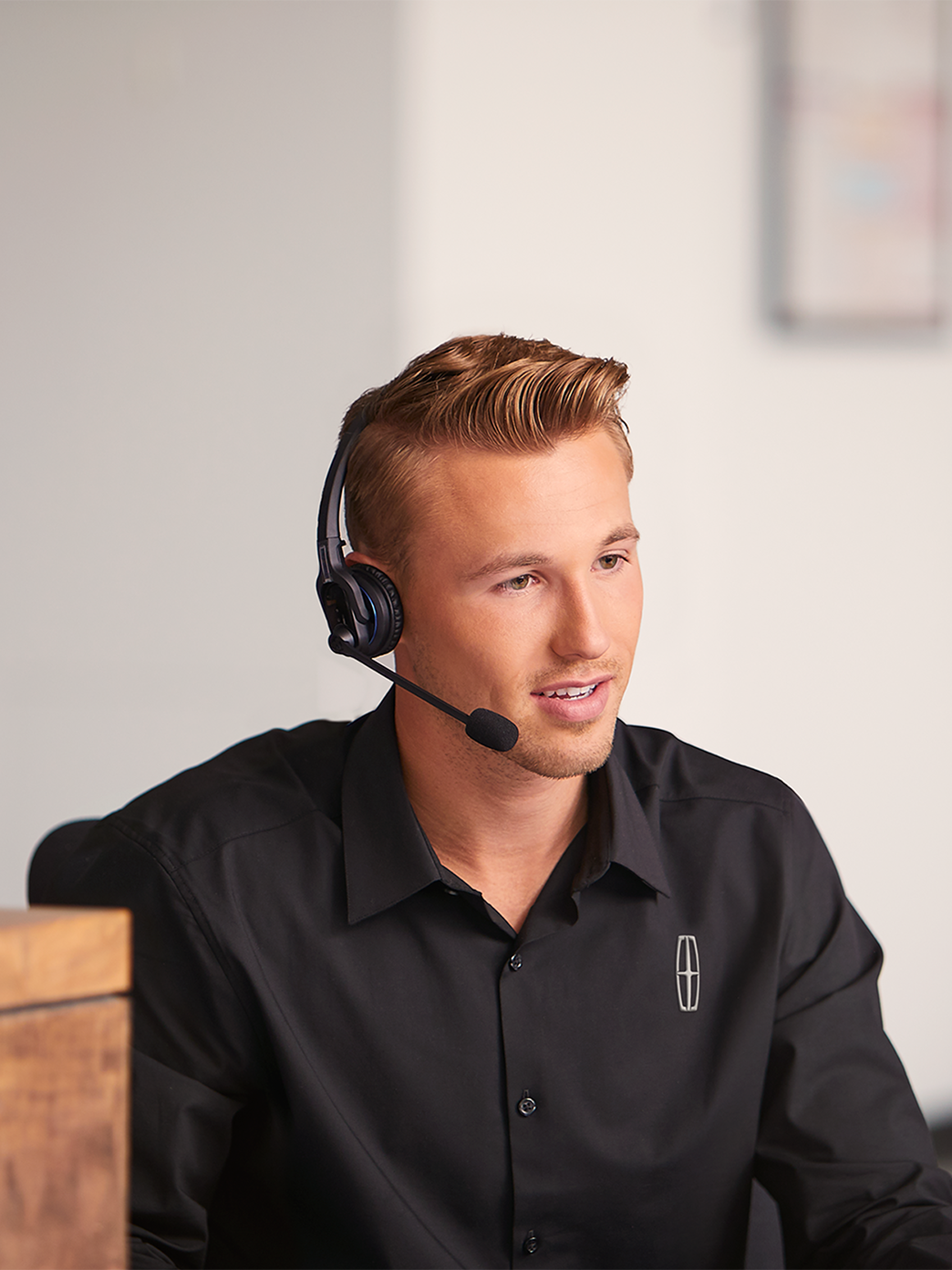 A support agent in a headset types at a desk with the Lincoln logo visible in the background