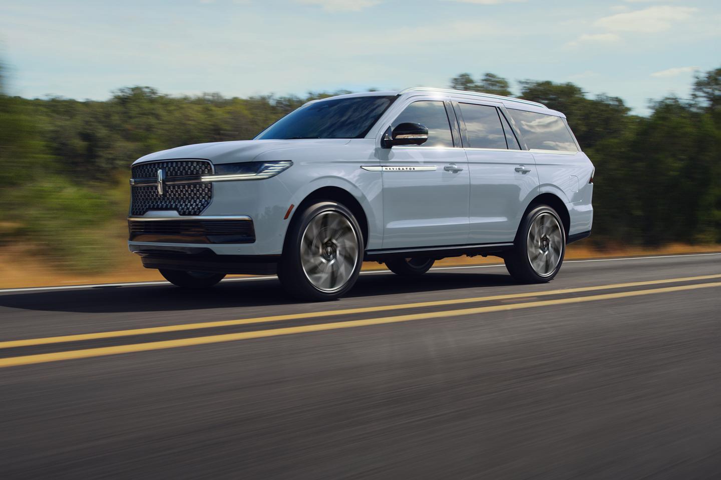 White Lincoln Navigator SUV driving on a scenic road with trees in the background.