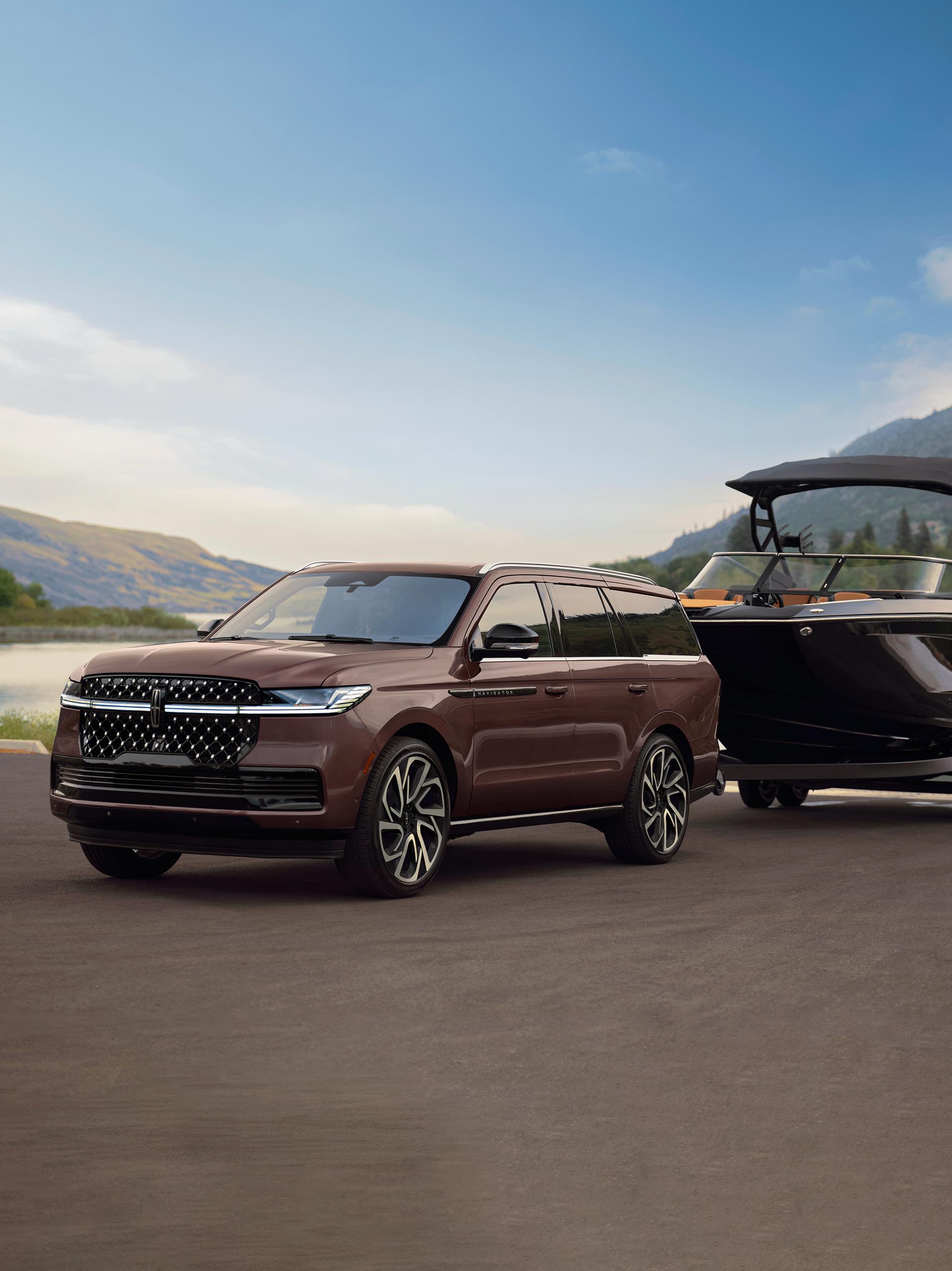 A 2027 Lincoln Navigator® SUV with a boat on a trailer is parked at a scenic boat ramp