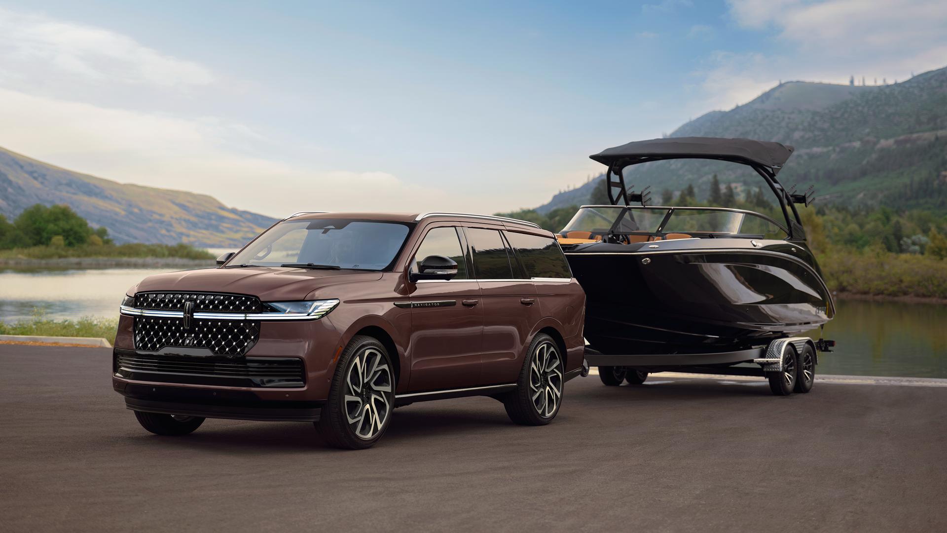 A 2027 Lincoln Navigator® SUV with a boat on a trailer is parked at a scenic boat ramp