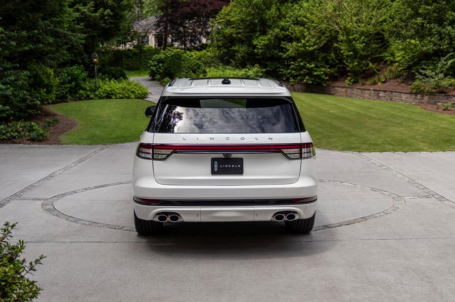 A white Lincoln SUV parked on a circular concrete driveway, surrounded by a lush, wooded residential landscape.