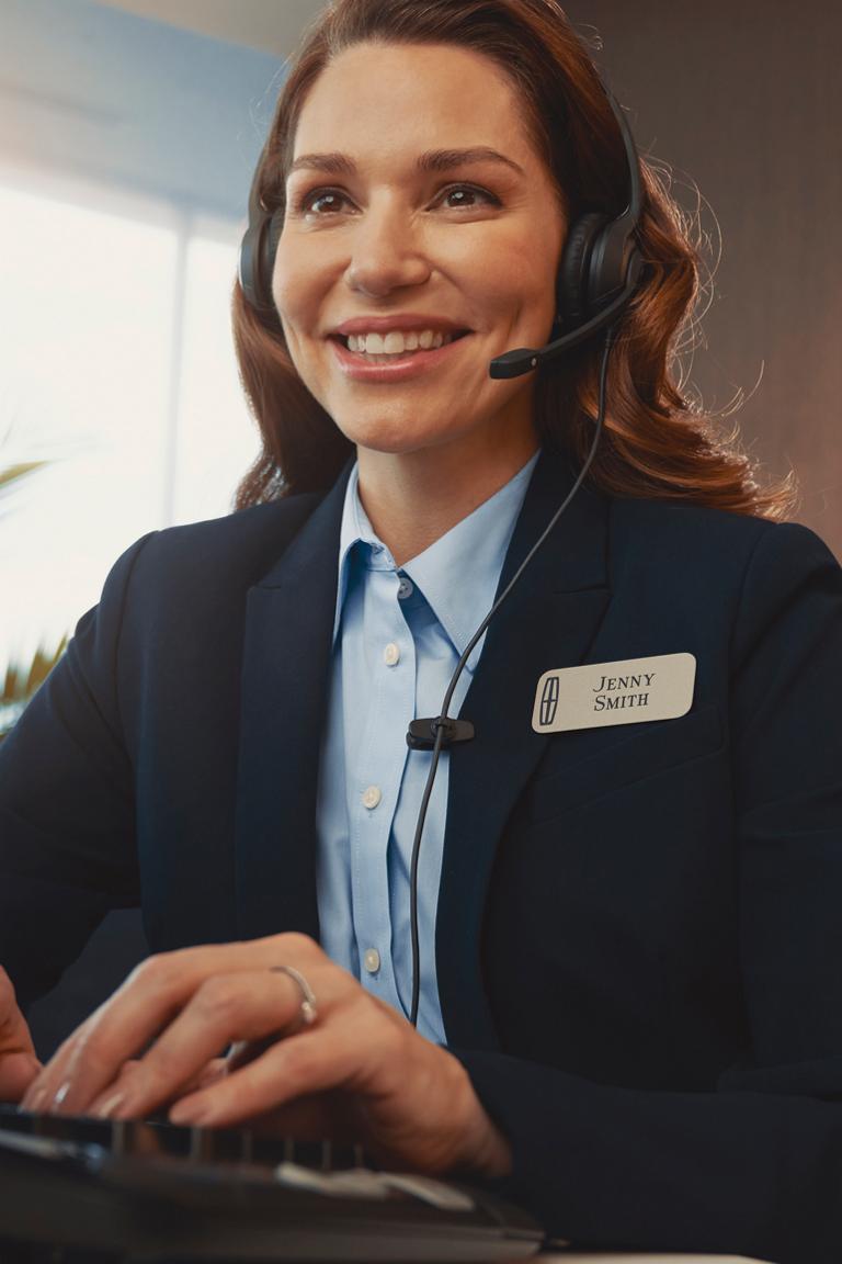 A support agent in a headset types at a desk with the Lincoln logo visible in the background