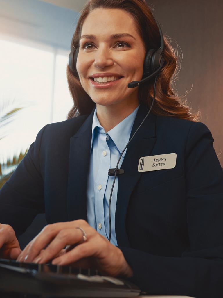 A support agent in a headset types at a desk with the Lincoln logo visible in the background