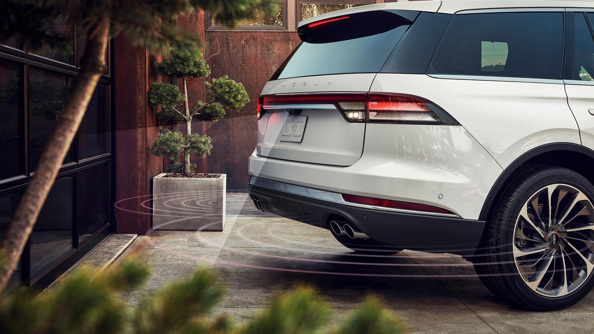 A 2027 Lincoln Aviator® is reversing towards a garage with simulated radar beams