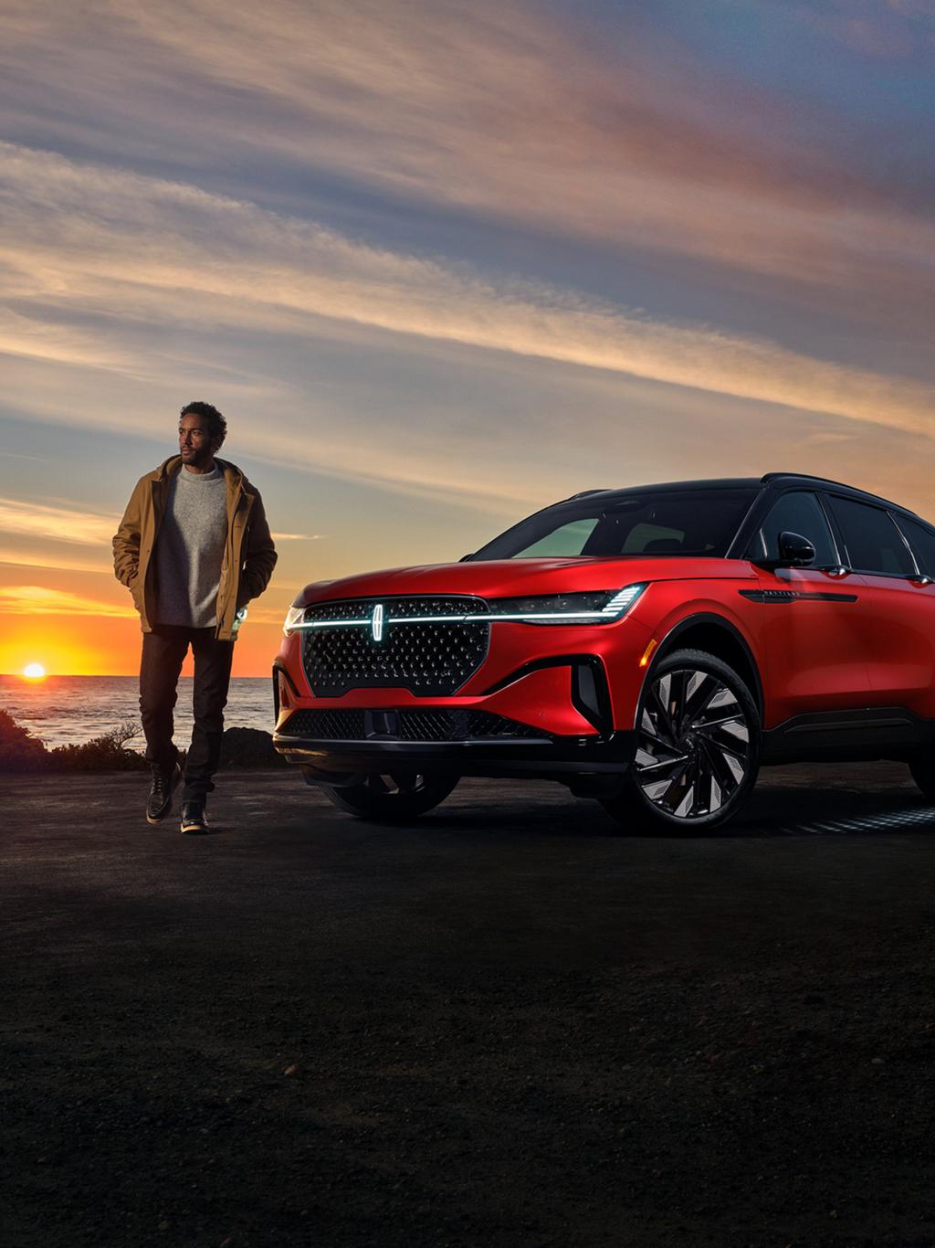 A man standing outside a Lincoln Nautilus parked near a body of water.