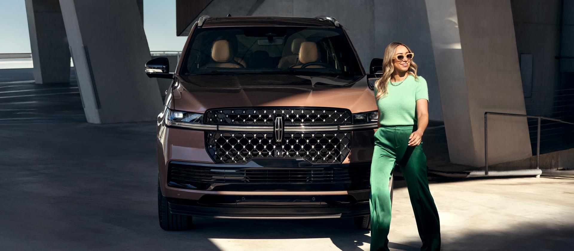A woman walking in front of a Lincoln vehicle.