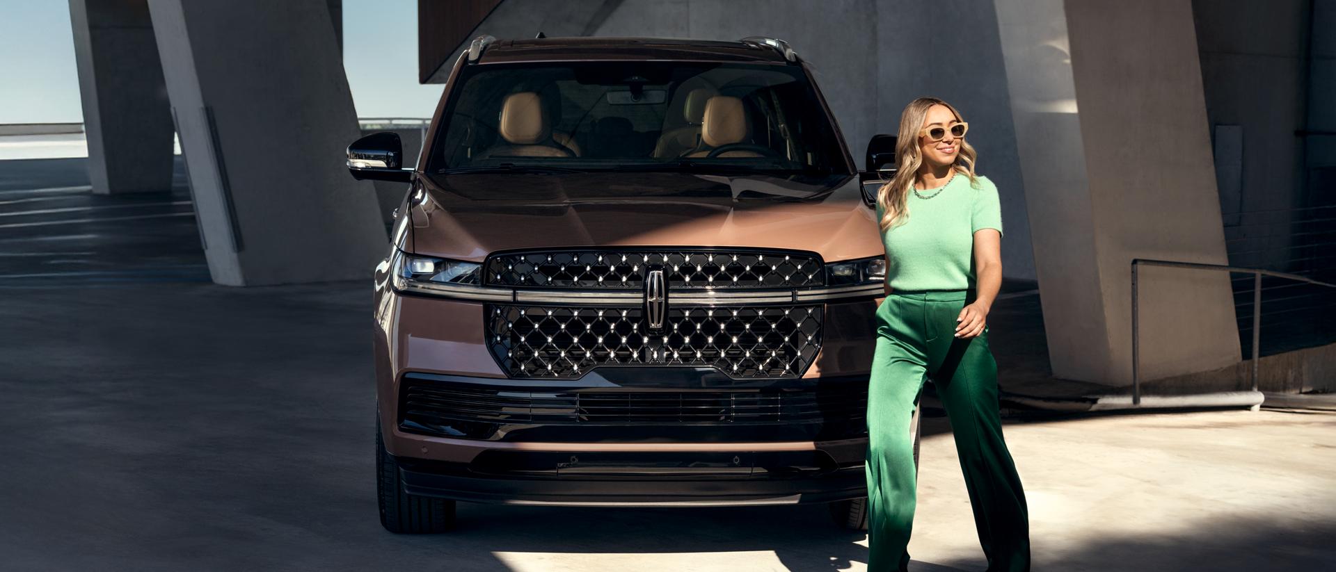 A woman walking infront of a Lincoln vehicle.
