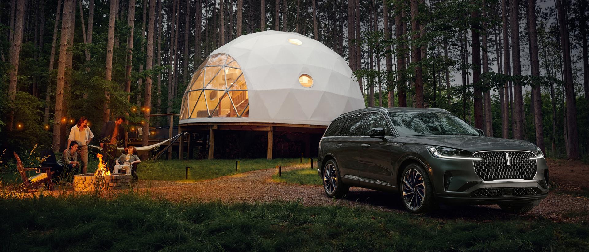 A 2027 Lincoln Aviator® is parked next to a luxury camping site as a family enjoys a campfire together