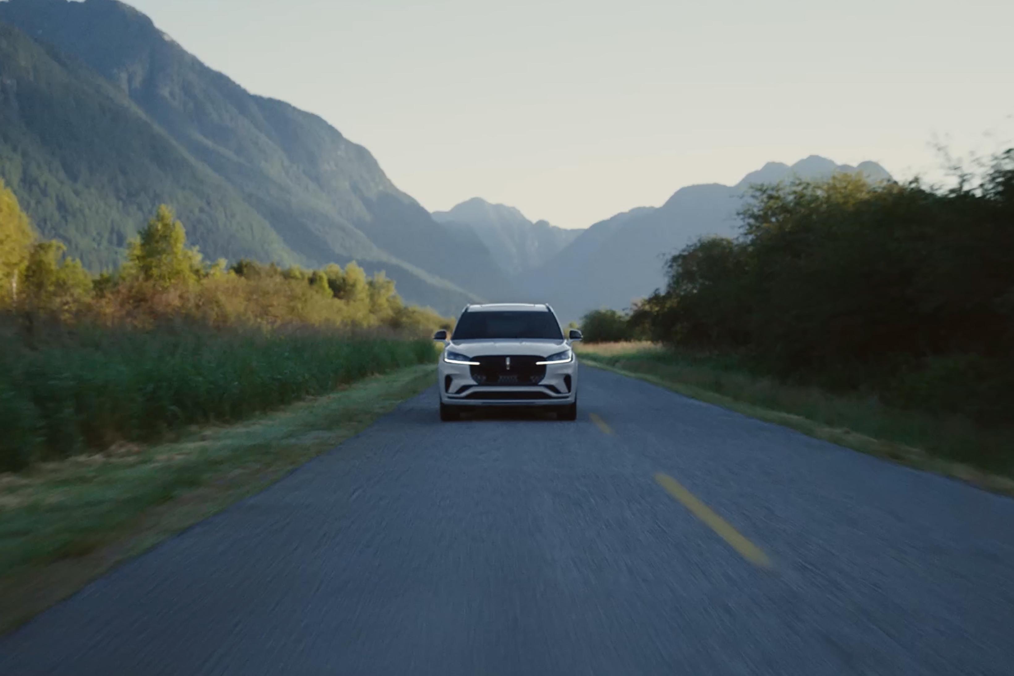 A 2027 Lincoln Aviator® is being driven on a highway surrounded by mountains in the background