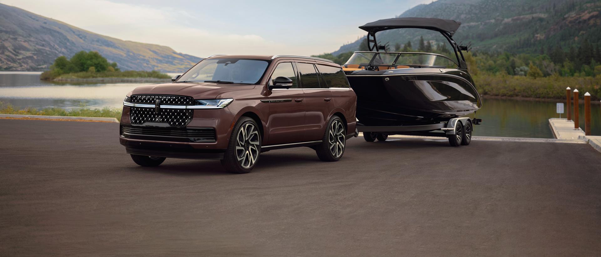 A 2027 Lincoln Navigator® SUV with a boat on a trailer is parked at a scenic boat ramp