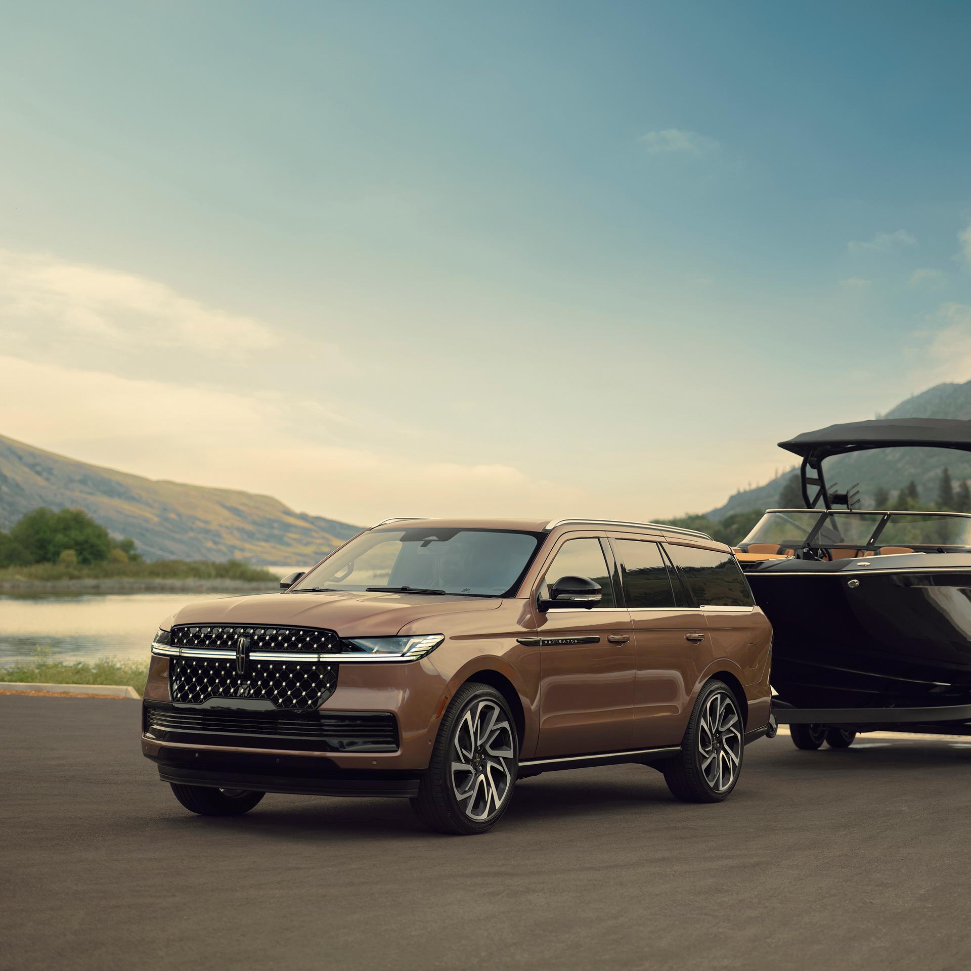 A 2026 Lincoln Navigator® Black Label vehicle is parked in front of a scenic waterfront with a pleasure boat hitched up