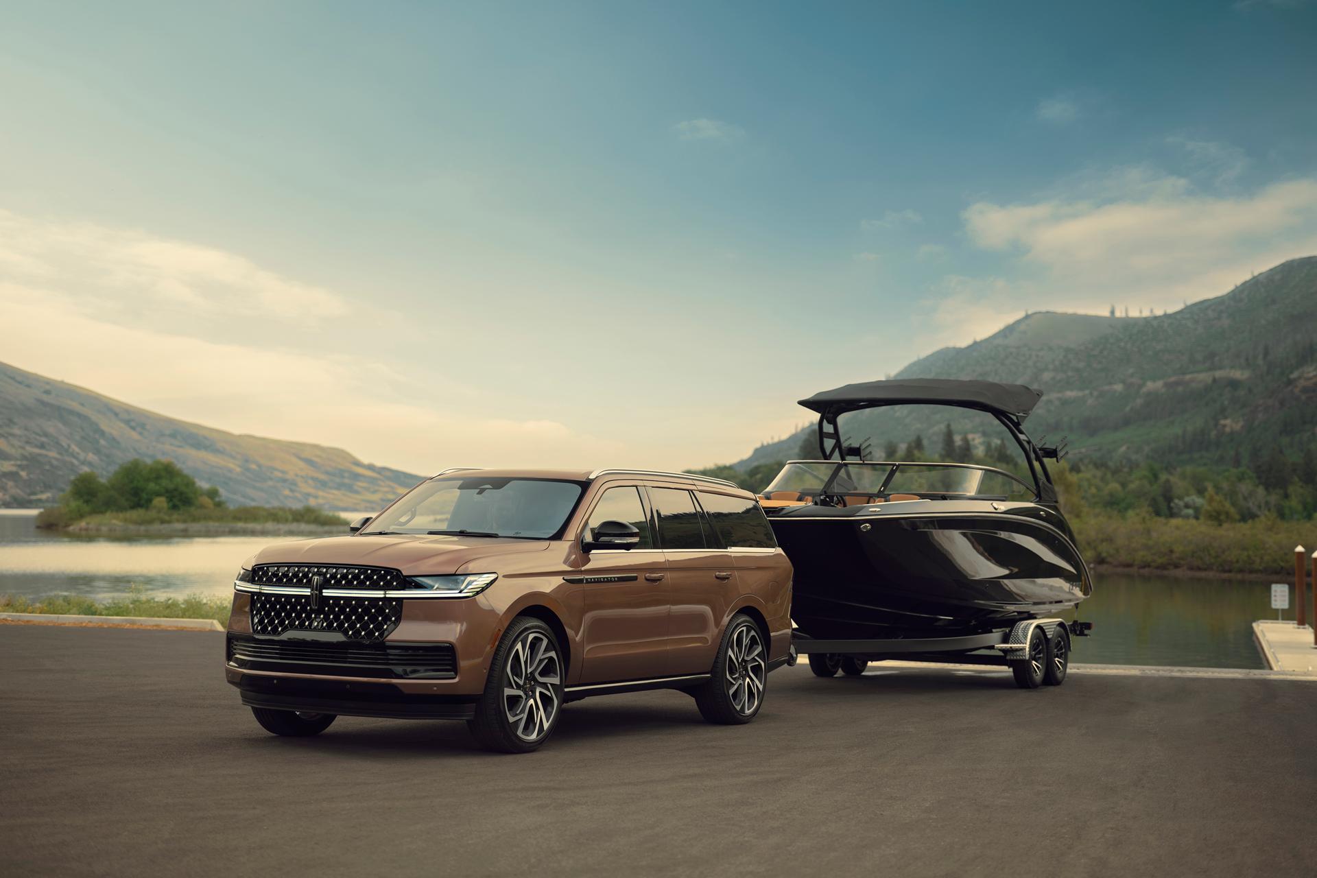 A 2026 Lincoln Navigator® Black Label vehicle is parked in front of a scenic waterfront with a pleasure boat hitched up