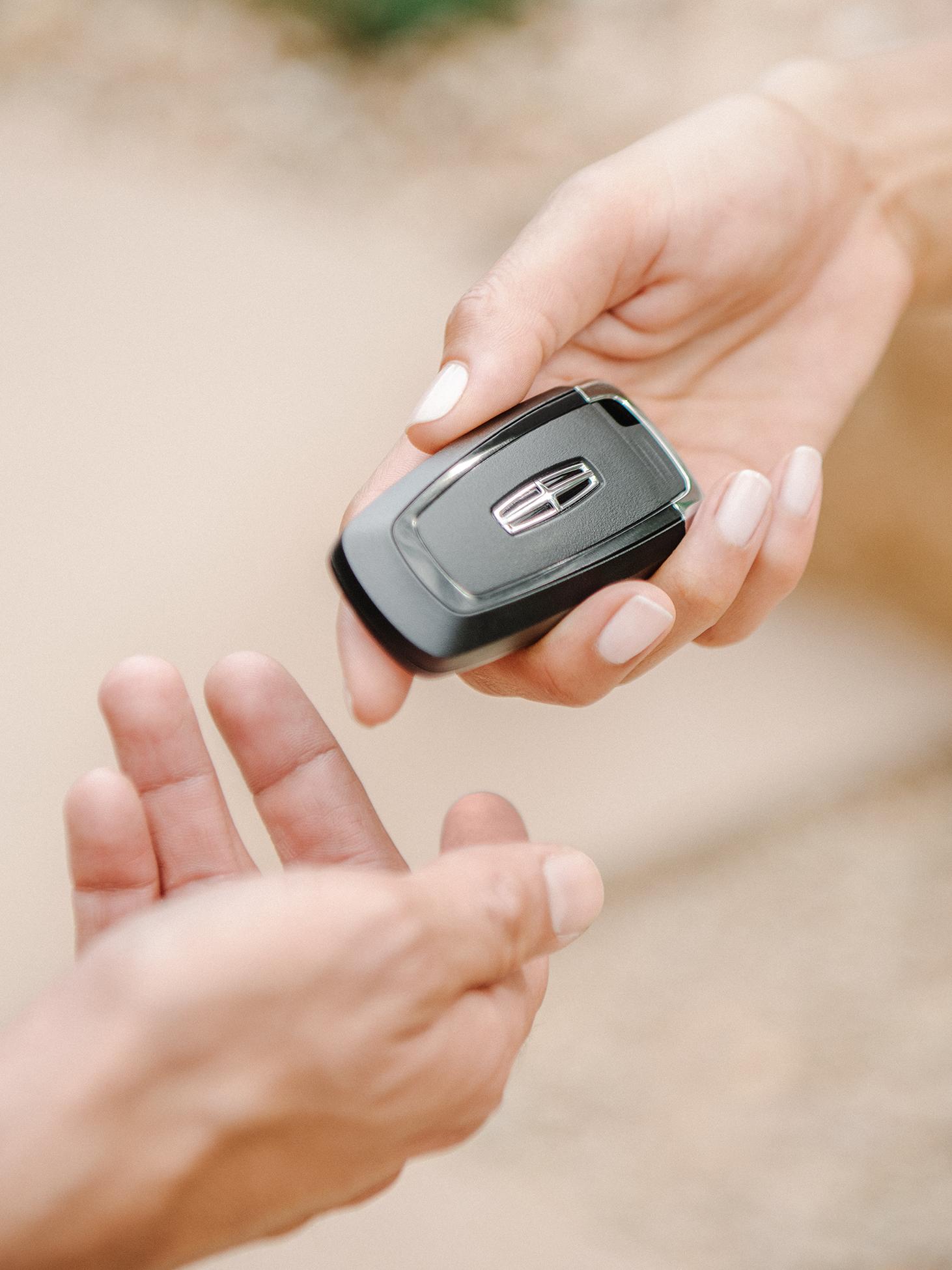 Close-up of a hand holding a Lincoln key fob to pass it to another person.