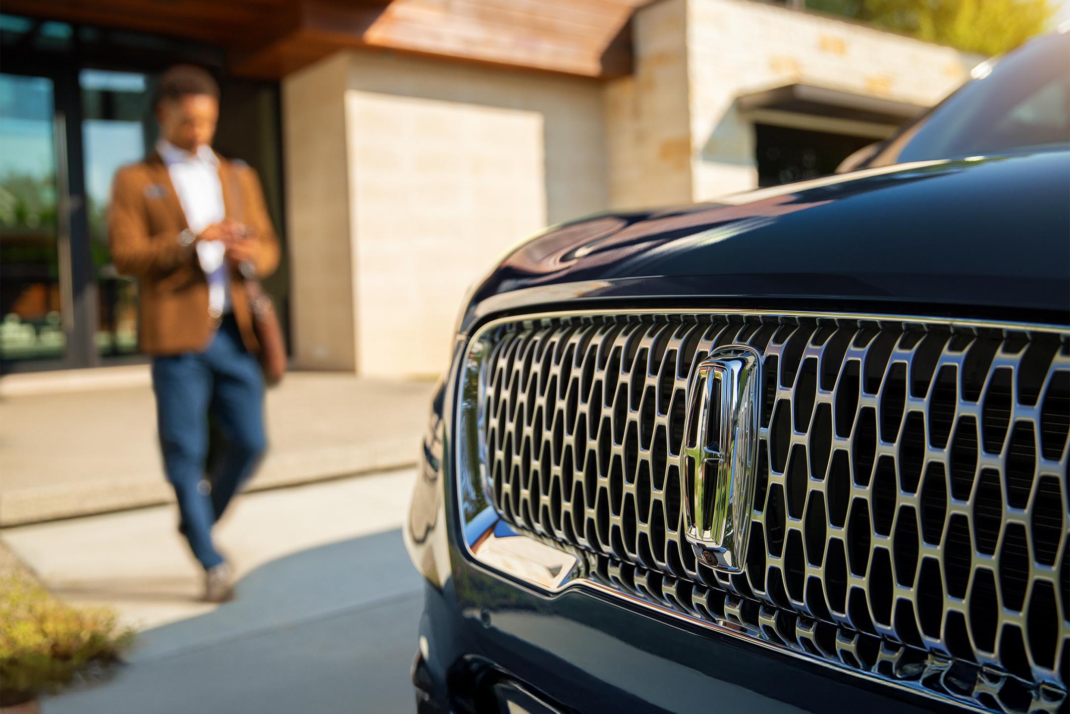 Close-up of a Lincoln vehicle grille with a person walking in the background.