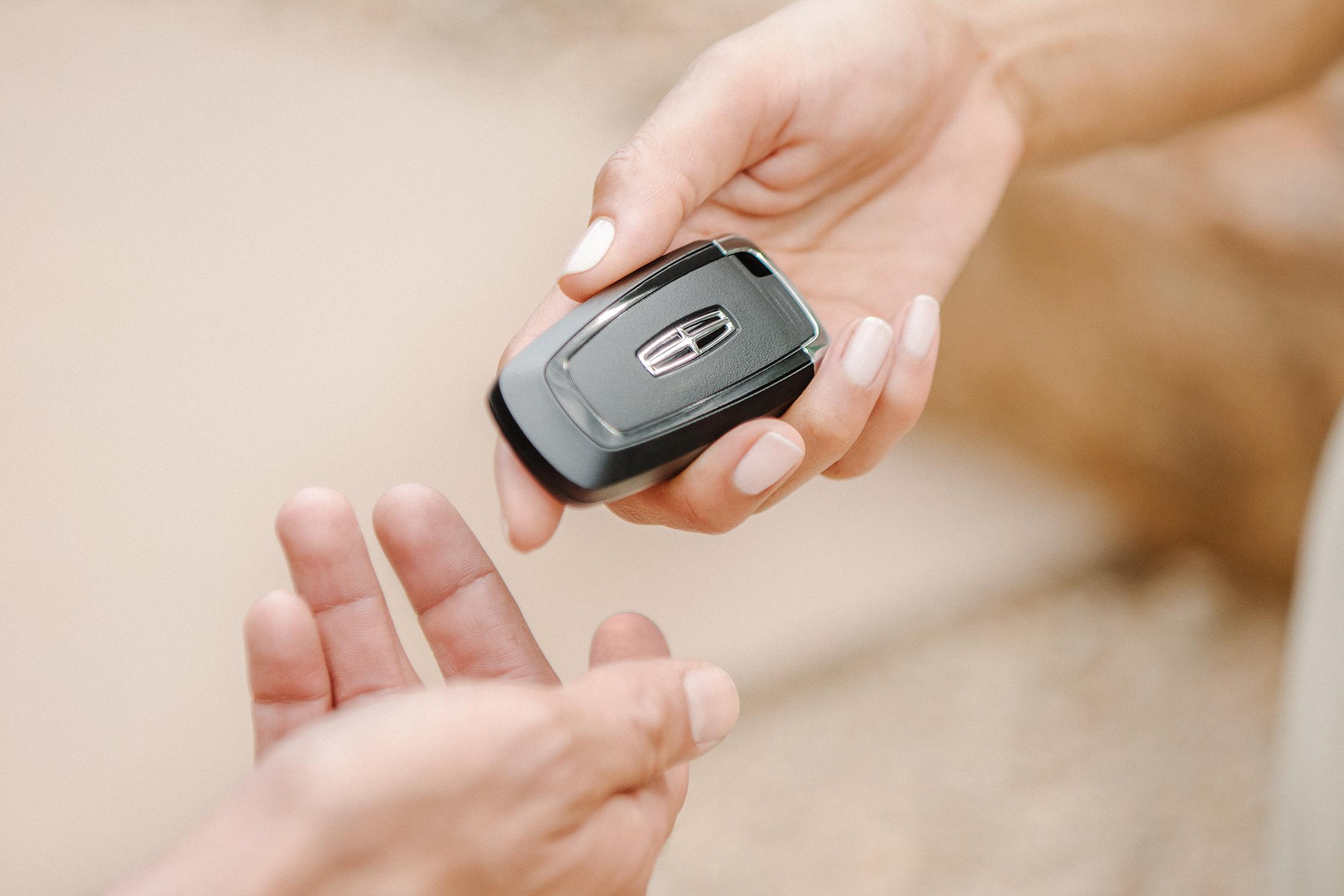 Close-up of a hand holding a Lincoln key fob to pass it to another person.